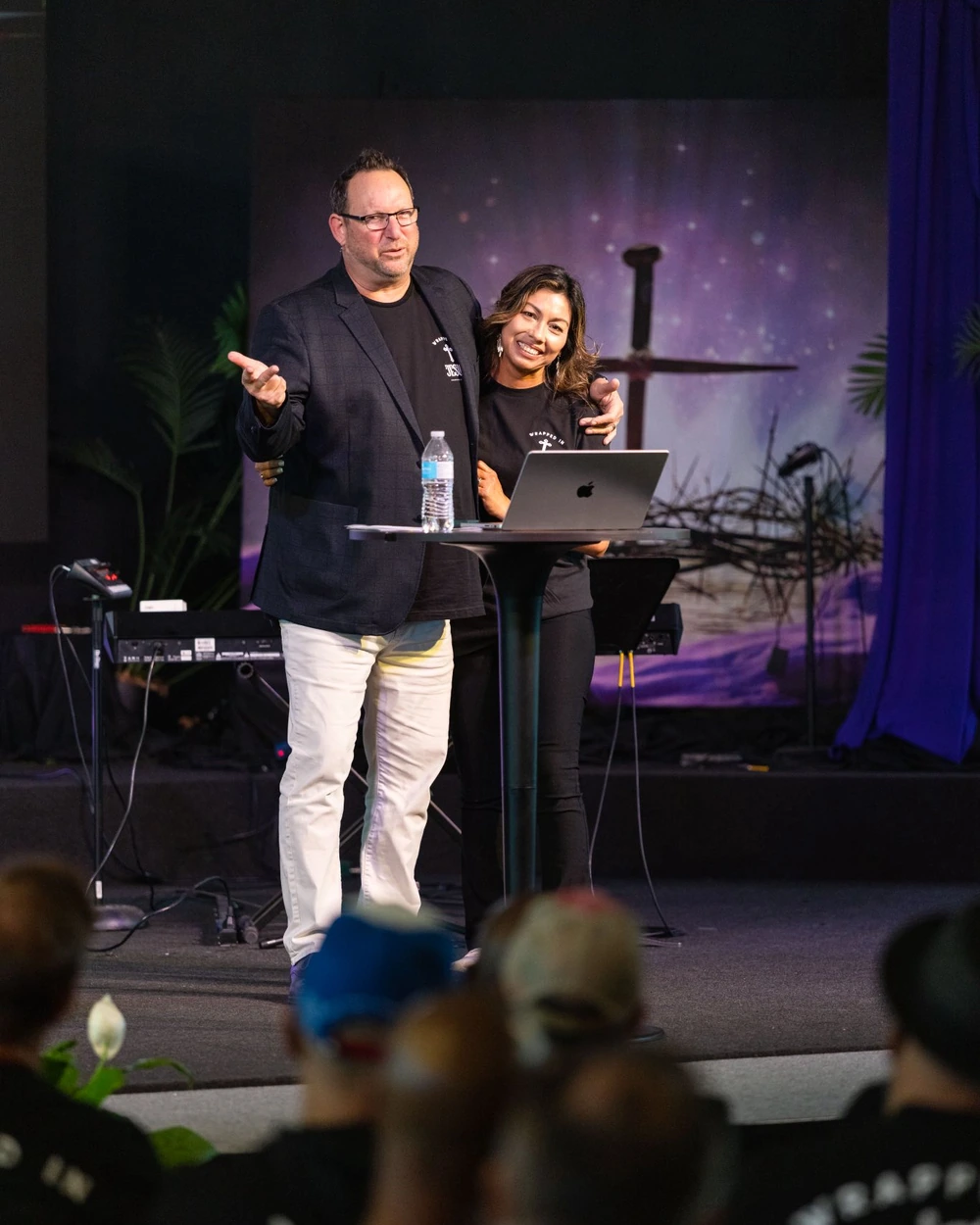 Michael Fineman speaking on stage beside his wife, the audience in the foreground